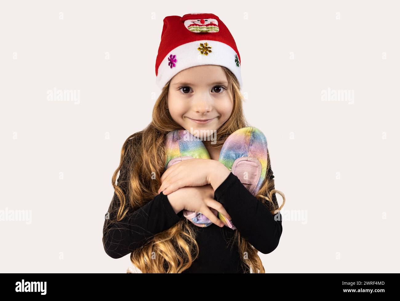 Il ritratto di una tenera ragazza ginnasta vestita con una tuta nera e con un cappello di Babbo Natale sulla testa abbraccia le ballerine. Concetto di amore per lo sport e. Foto Stock