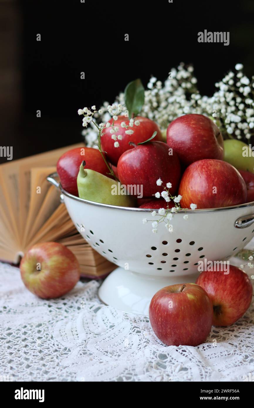 Mele rosse luccicanti, fiori bianchi di Gypsophila e libro aperto su un tavolo. Sfondo nero con spazio di copia. Mangiare un concetto fresco. Foto Stock