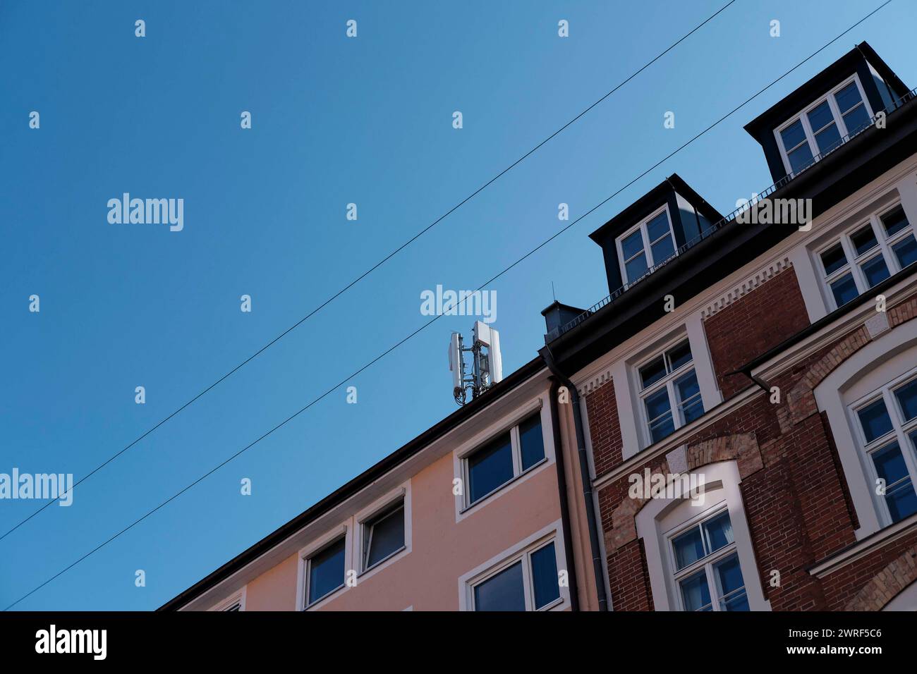 Mobilfunkmast auf Hausdach Mobilfunkmast auf Hausdach a München Maxvorstadt. Bildlich umrahmt von Stromleitungen der hängenden Straßenbeleuchtung Mün Foto Stock