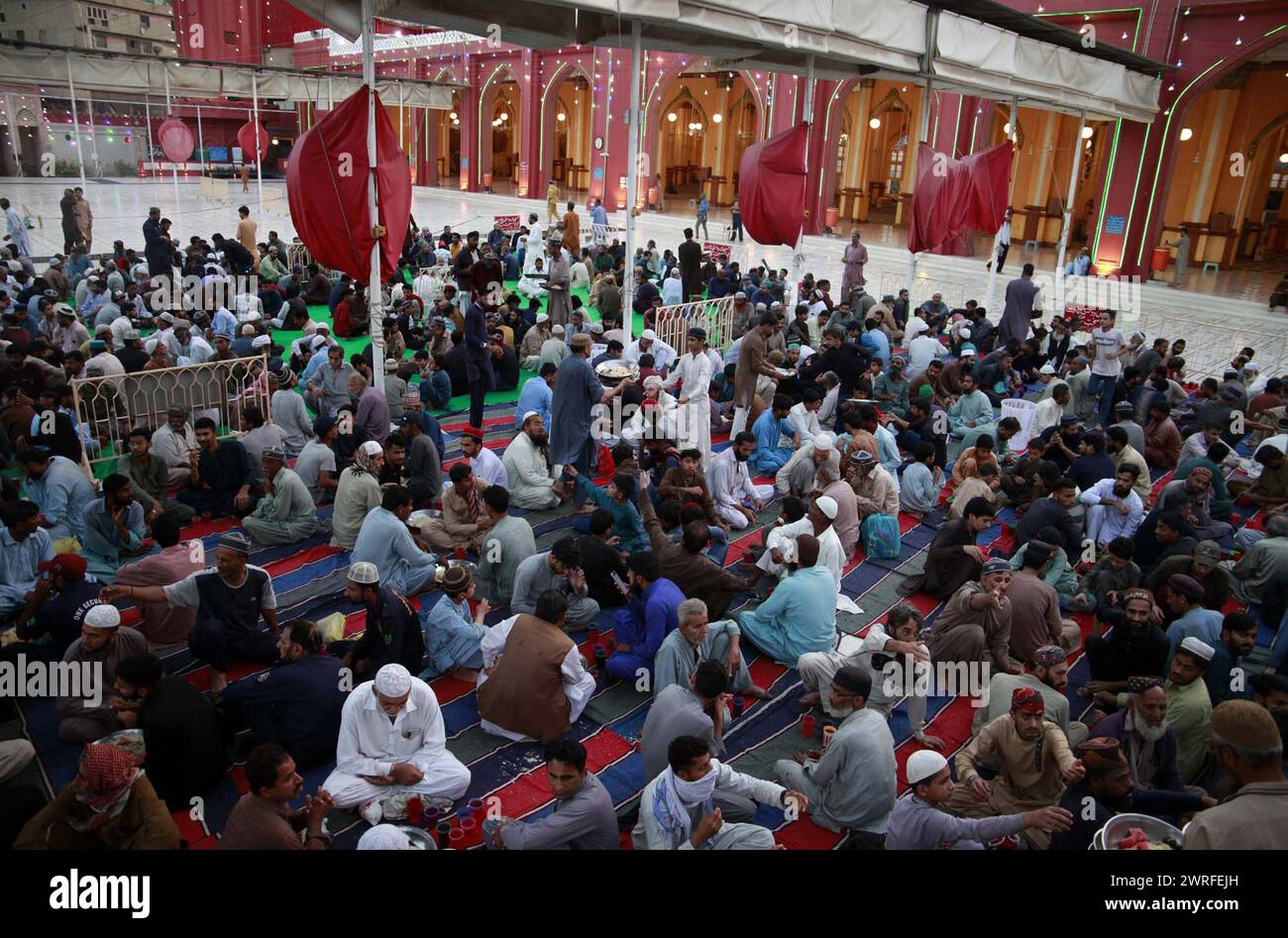 I fedeli musulmani siedono per Iftar (pasto veloce), durante il primo giorno del mese Santo di Ramadan-ul-Mubarak alla Moschea New Memon di Karachi martedì 12 marzo 2024. Foto Stock
