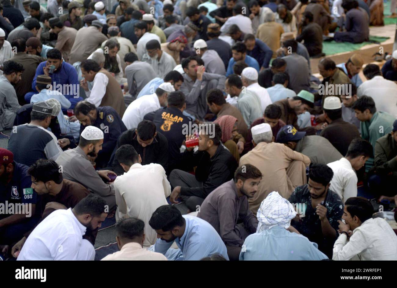 I fedeli musulmani siedono per Iftar (pasto veloce), durante il primo giorno del mese Santo di Ramadan-ul-Mubarak alla Moschea New Memon di Karachi martedì 12 marzo 2024. Foto Stock