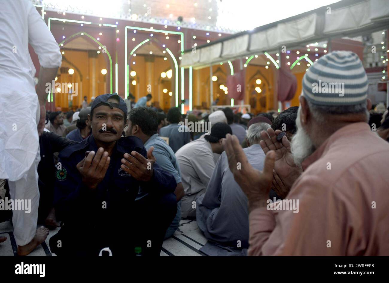 I fedeli musulmani siedono per Iftar (pasto veloce), durante il primo giorno del mese Santo di Ramadan-ul-Mubarak alla Moschea New Memon di Karachi martedì 12 marzo 2024. Foto Stock