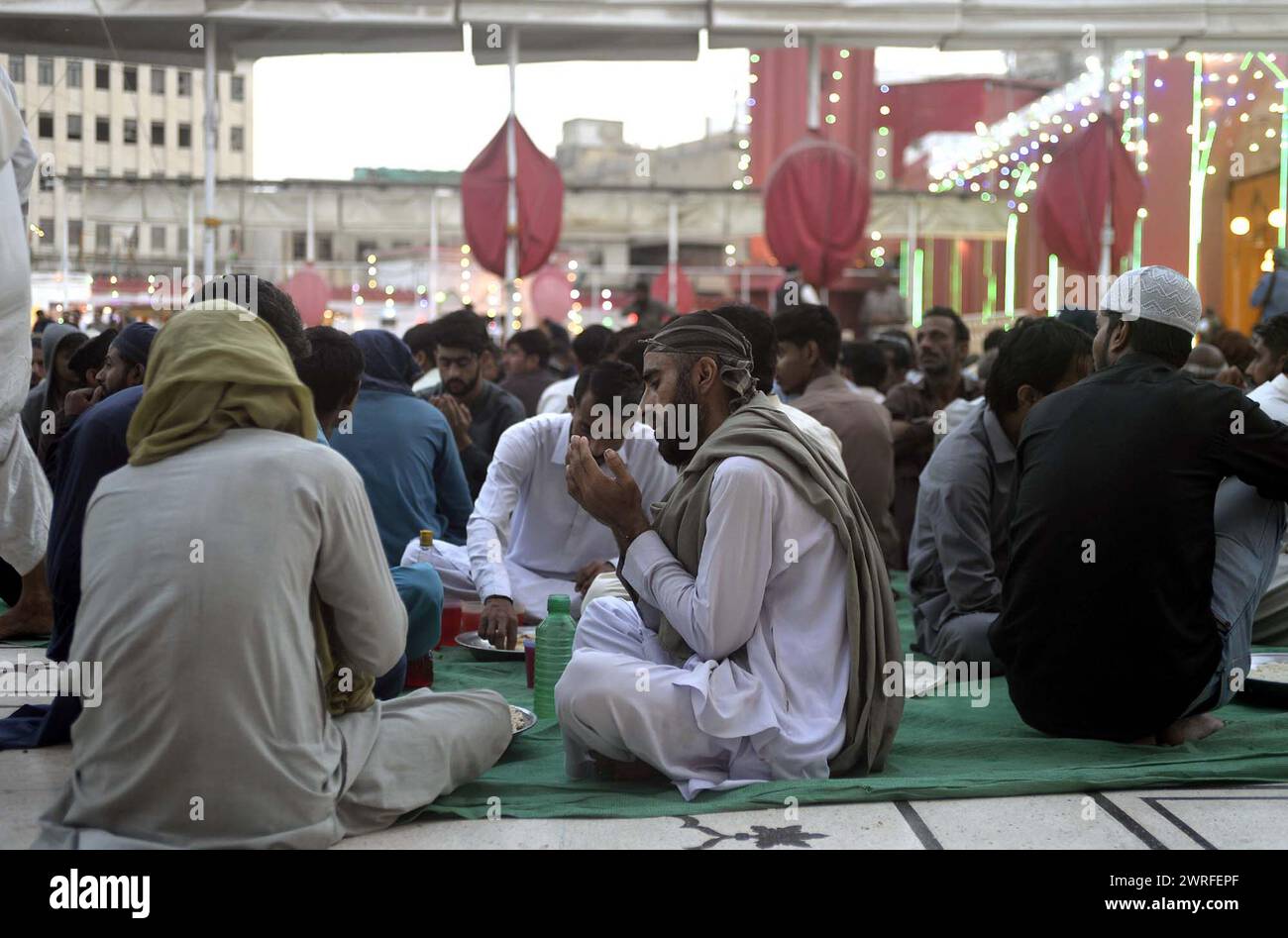 I fedeli musulmani siedono per Iftar (pasto veloce), durante il primo giorno del mese Santo di Ramadan-ul-Mubarak alla Moschea New Memon di Karachi martedì 12 marzo 2024. Foto Stock