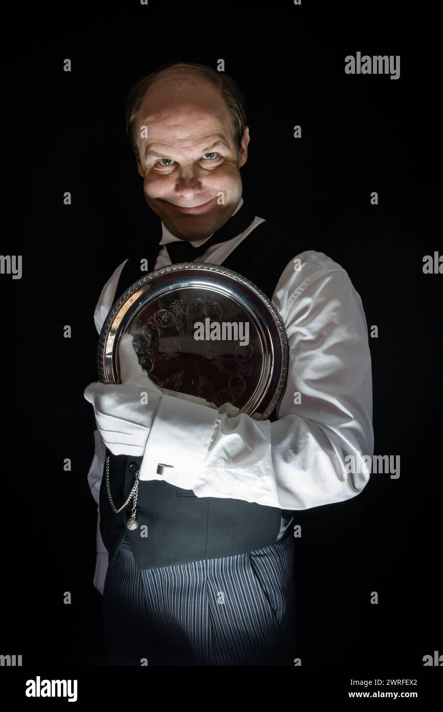 Ritratto di un maggiordomo inquietante con un sorriso raccapricciante che regge il vassoio da portata in argento. Il concetto del Butler CE l'ha fatta. Foto Stock