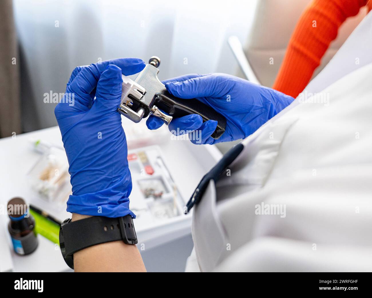 Cosmetologa donna carica la pistola perforante con orecchini medici in un salone di cosmetologia su uno sfondo con strumenti per un processo di perforazione di successo. Foto Stock