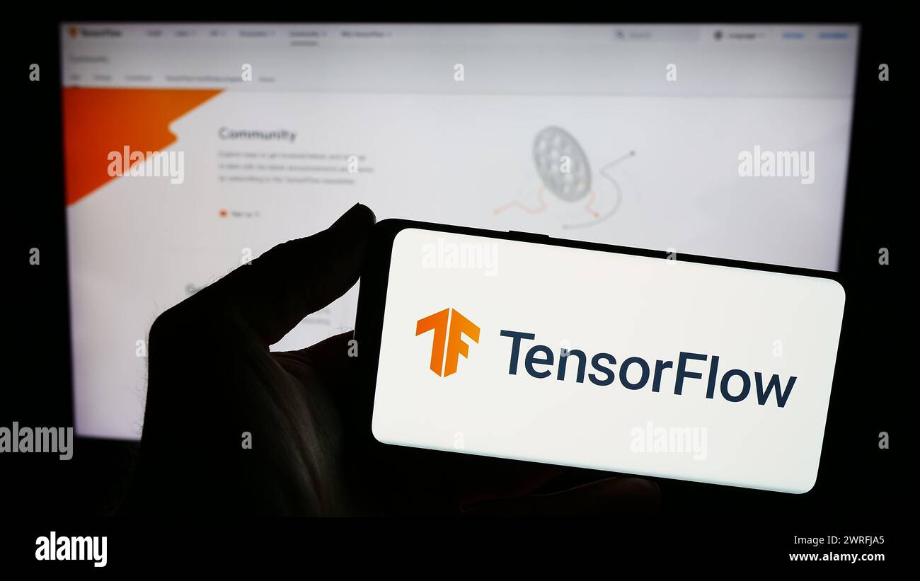 Persona che possiede uno smartphone con il logo della libreria software open source TensorFlow davanti al sito Web. Mettere a fuoco il display del telefono. Foto Stock