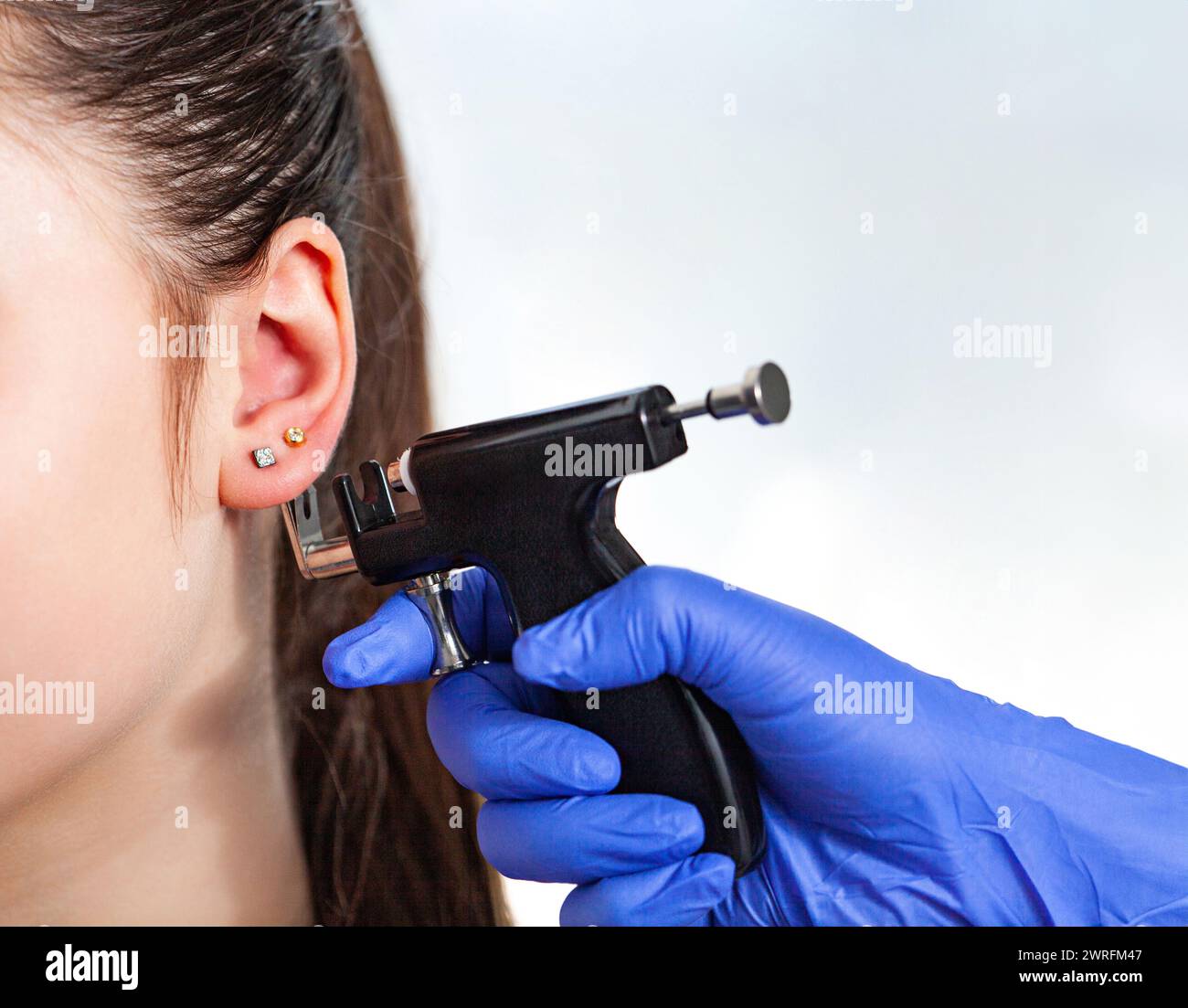 Donna che ha orecchio piercing processo con pistola perforante speciale in centro di bellezza da operatore medico, ritagliato vista ravvicinata. Foto di alta qualità Foto Stock