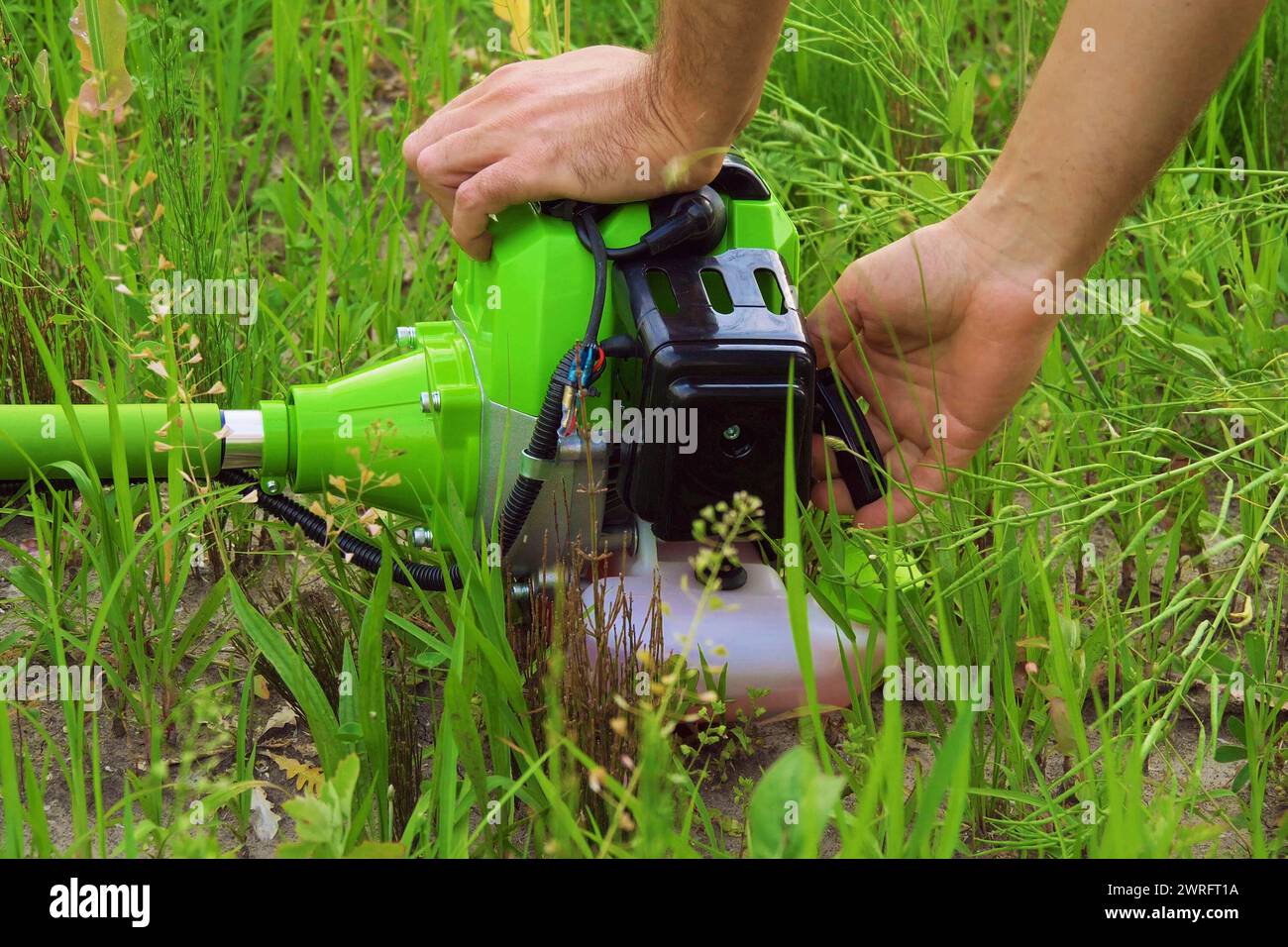 Mano maschile che avvia un rasaerba su sfondo erba. Il giardiniere avvia il rasaerba. Il rasaerba professionale avvia il suo nuovo tagliaerba a gas. Il lavoratore avvia il rasaerba in un prato con erba. Foto Stock