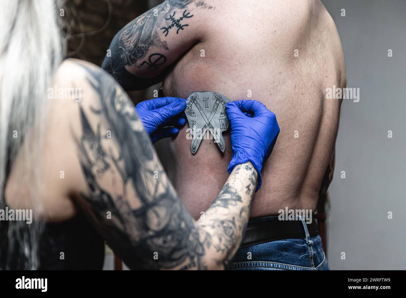 Primo piano orizzontale di un tatuatore che applica uno stencil trasferibile di uno stemma sul corpo di un cliente. Concetto di business, arte. Foto Stock