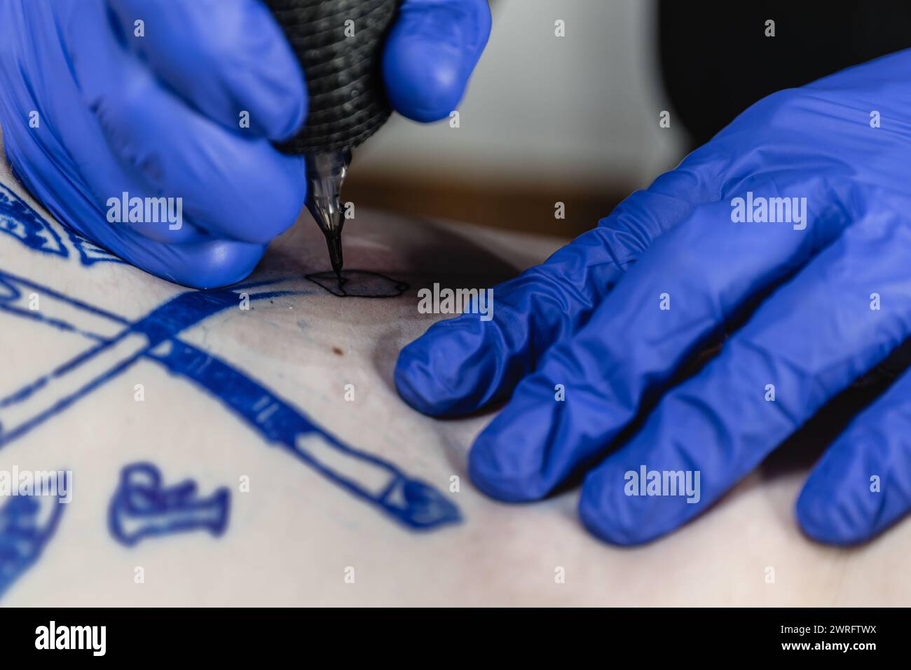 Foto orizzontale l'ago di una macchina per tatuaggi delinea delicatamente uno stemma, guidato dalla mano ferma del tatuatore. Concept business, Foto Stock