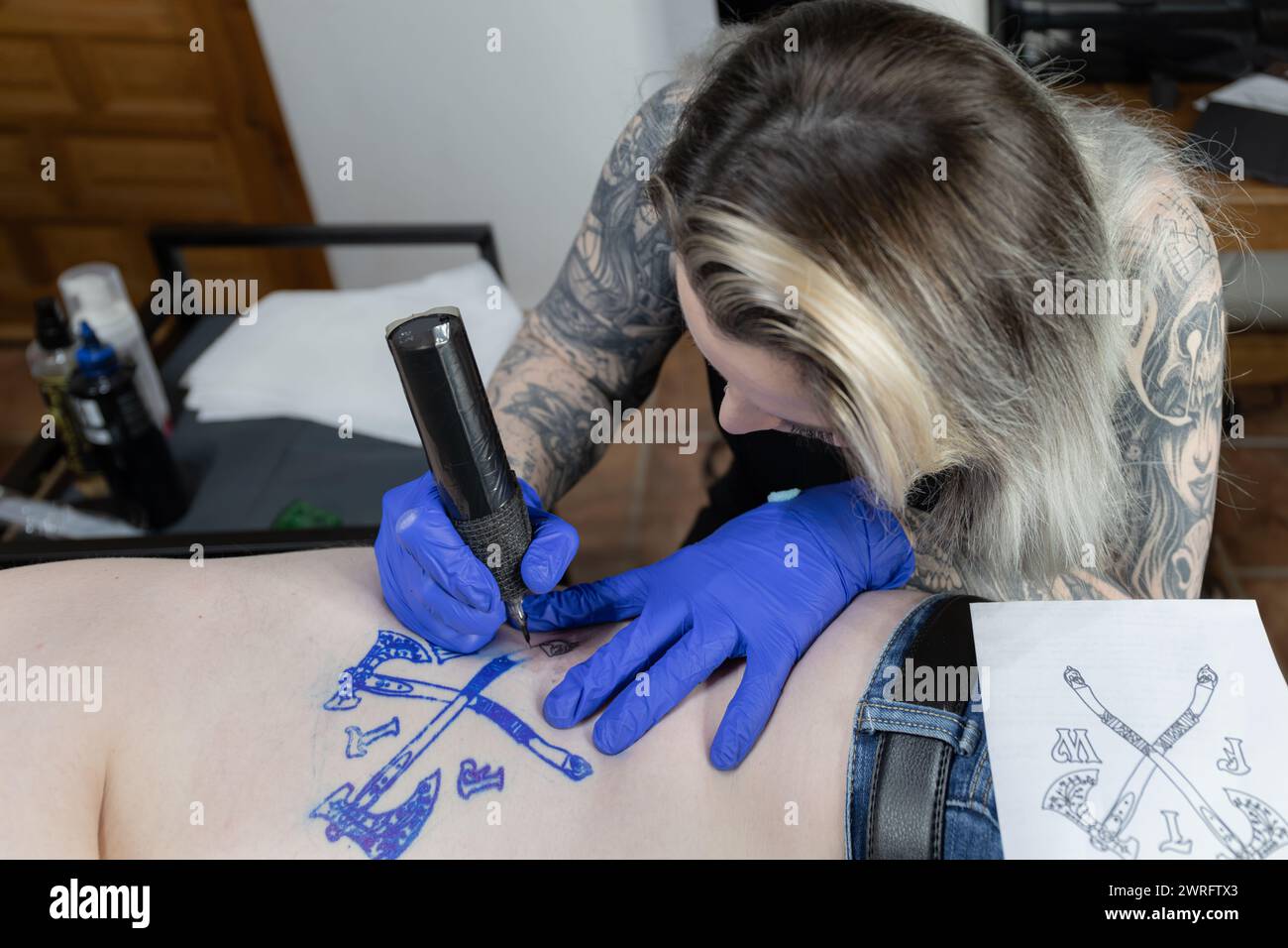 Foto orizzontale un tatuatore attento lavora su uno stemma, mostrando un mix di messa a fuoco e delicata abilità. Concetto di business, arte. Foto Stock