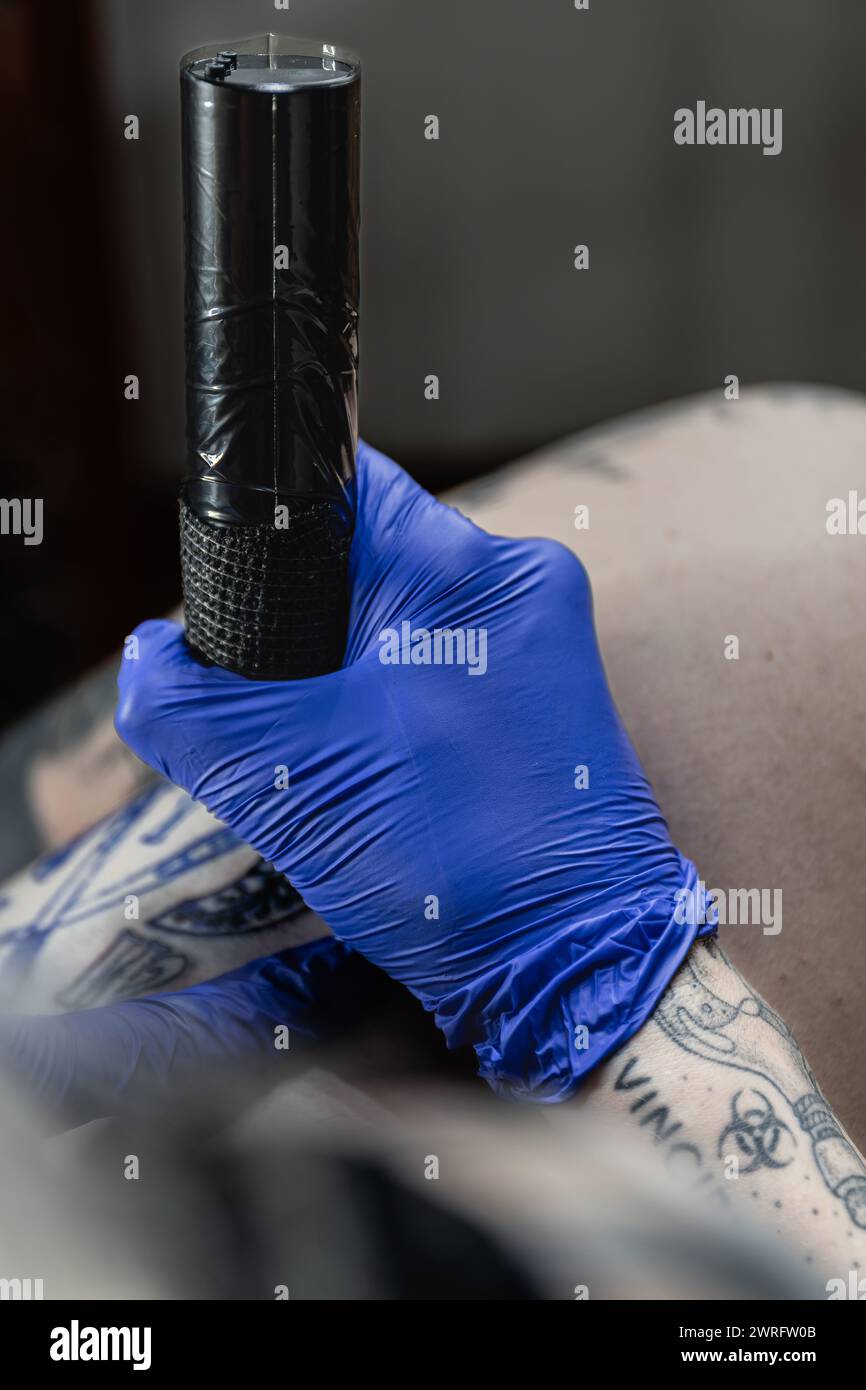Foto verticale un primo piano della mano indossata dai guanti di un tatuatore che afferrano la macchina per tatuaggi, pronta a creare un'arte permanente sulla pelle. Concetto di business, arte. Foto Stock