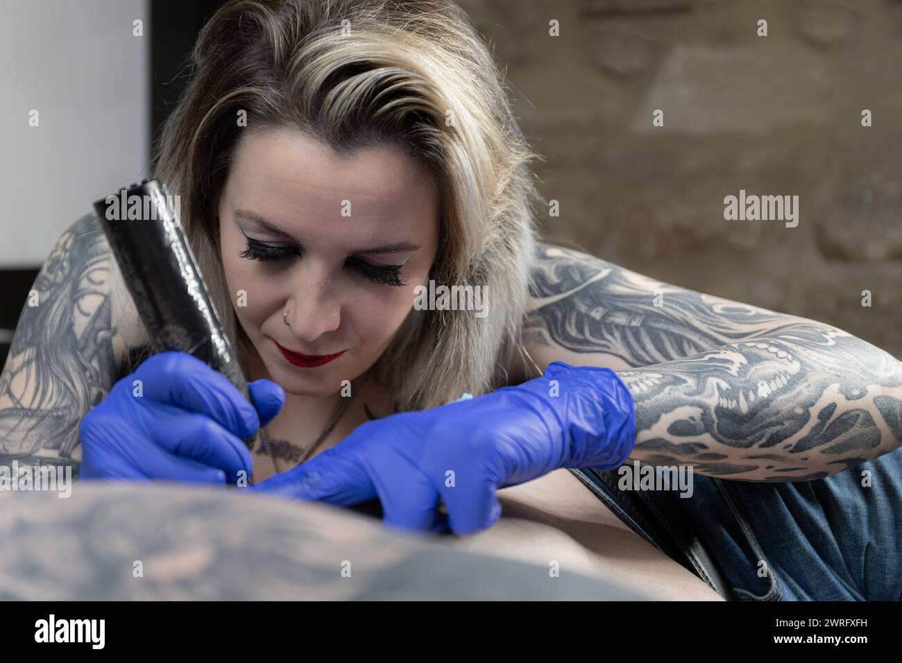 Foto orizzontale un abile tatuatore con elaborati tatuaggi sulle maniche incide con cura un nuovo design, incarnando l'arte del tatuaggio. Copia spazio. Foto Stock