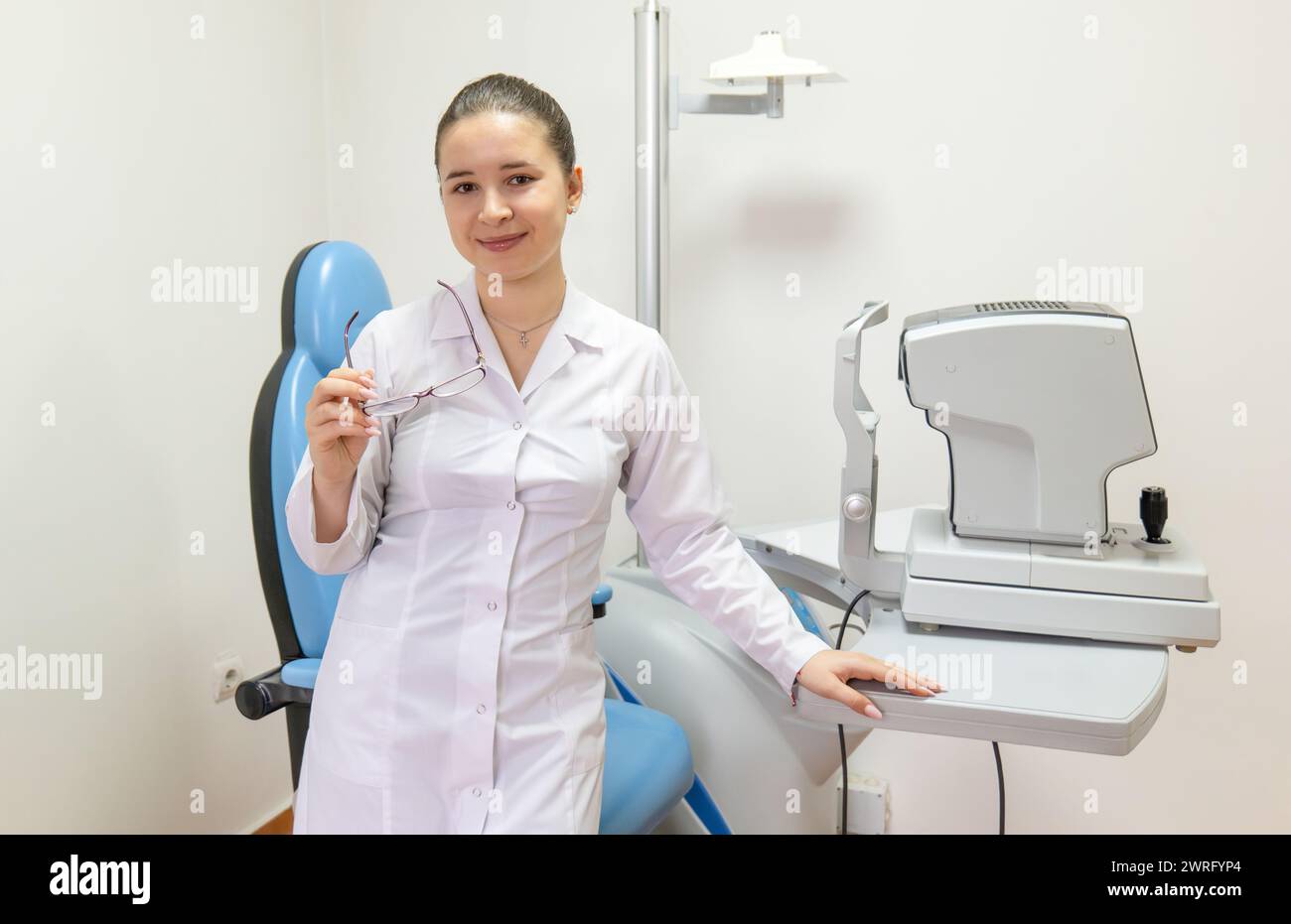 L'oculista è in piedi nella stanza, tenendo un paio di bicchieri con un sorriso. Il suo braccio è piegato al gomito, il pollice poggia sulla manica Foto Stock