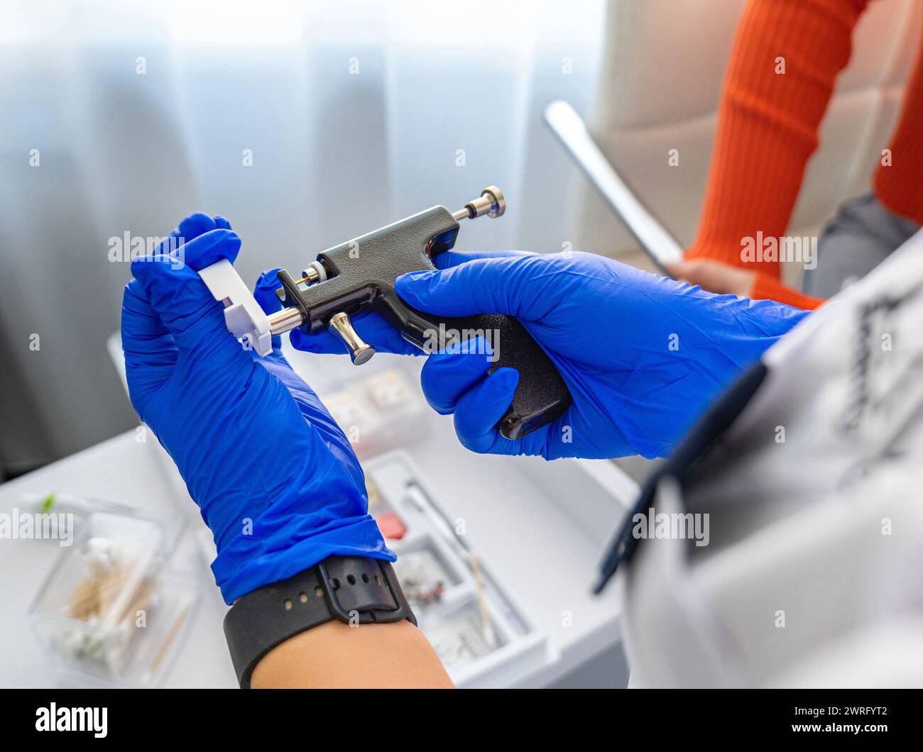 Cosmetologa donna in guanti monouso blu sterile carica la pistola perforante con orecchini medici in un salone di cosmetologia. Foto di alta qualità Foto Stock