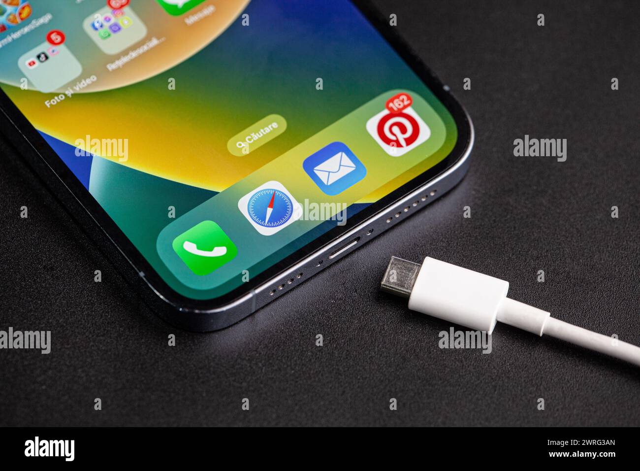 L'immagine dell'iPhone con il caricabatterie tipo c accanto, che è il cambiamento dell'anno nella tecnologia telefonica, su sfondo nero.Hincesti Foto Stock