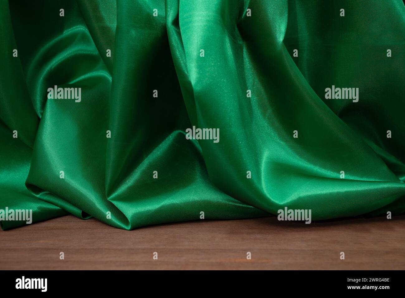 Pavimento in legno vuoto con eleganti tende in tessuto satinato verde ondulato, sfocate sullo sfondo, sfondo del posizionamento dei prodotti Foto Stock