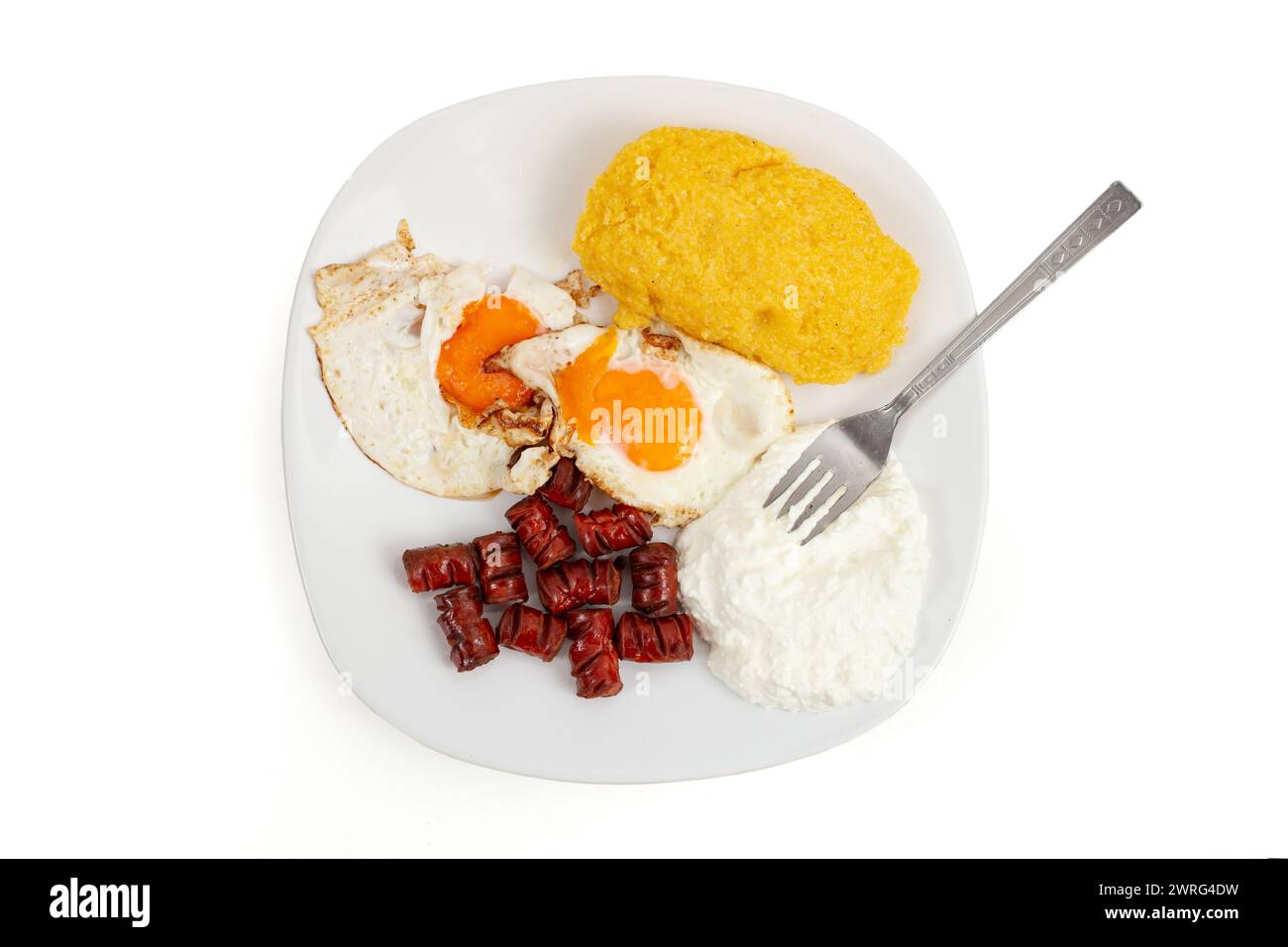 Polenta , uova fritte , salsicce e ricotta su un piatto bianco isolato su fondo bianco, piatte da vicino Foto Stock