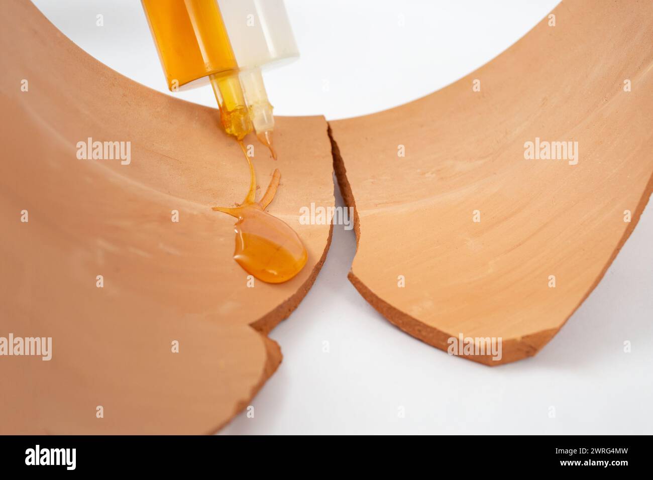 Siringa doppia con incollaggio in gel epossidico e versamento su frammenti di ceramica marrone rotti Foto Stock