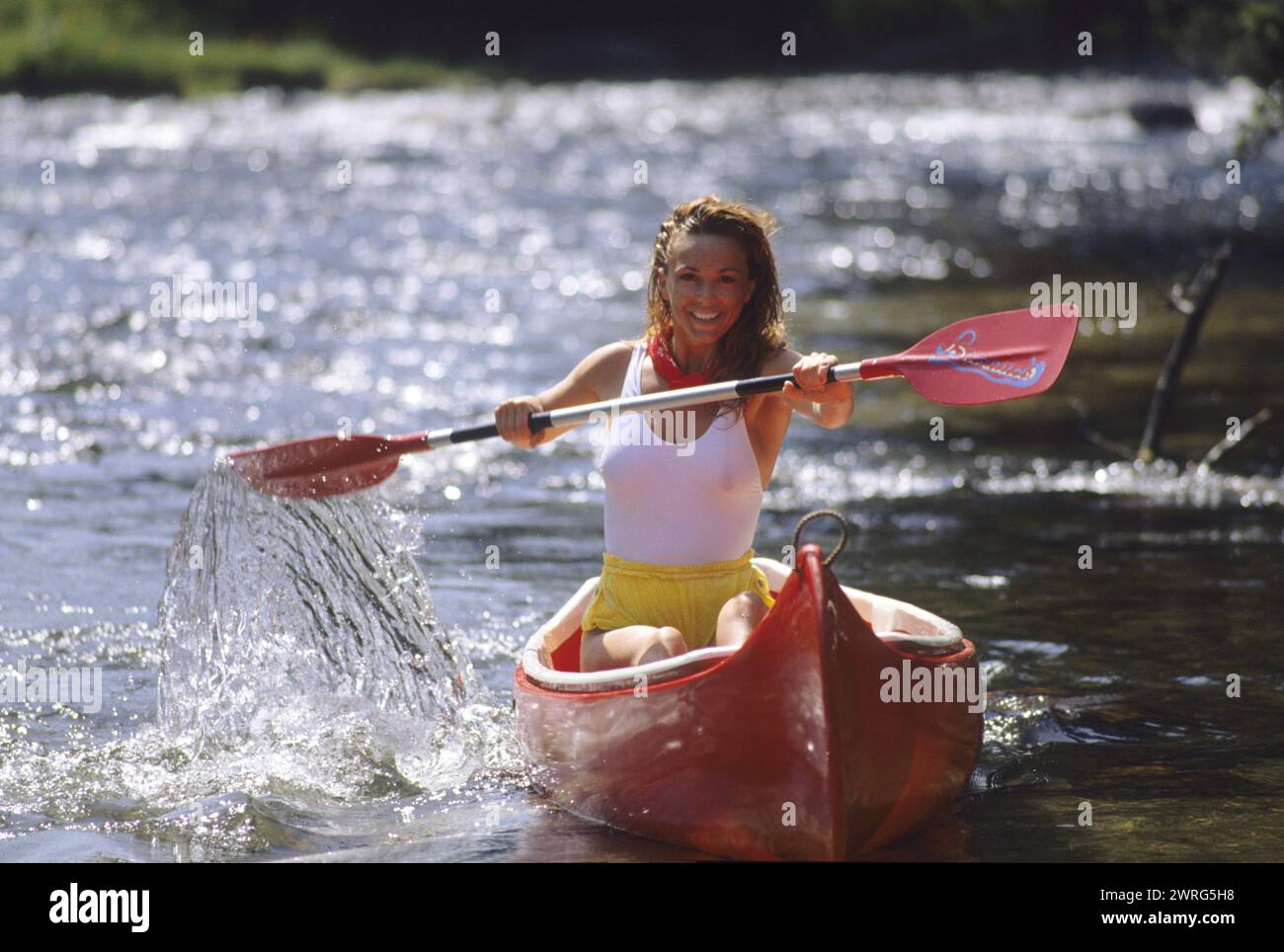 capelli biondi pretty woman fotocamera anteriore rossa dall'aspetto canoo felice faccia sorridente su un fogliame verde fiume sul retro Foto Stock