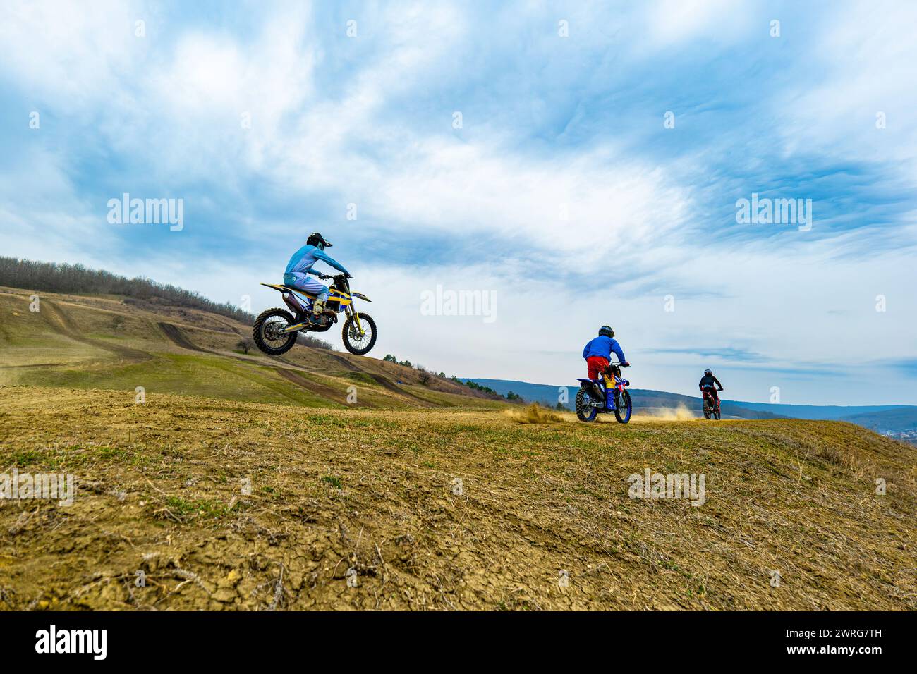 Due appassionati di motocross guidano motociclette su una strada sterrata sotto il cielo nuvoloso, indossando caschi e equipaggiamento protettivo. Le ruote sollevano polvere come Foto Stock