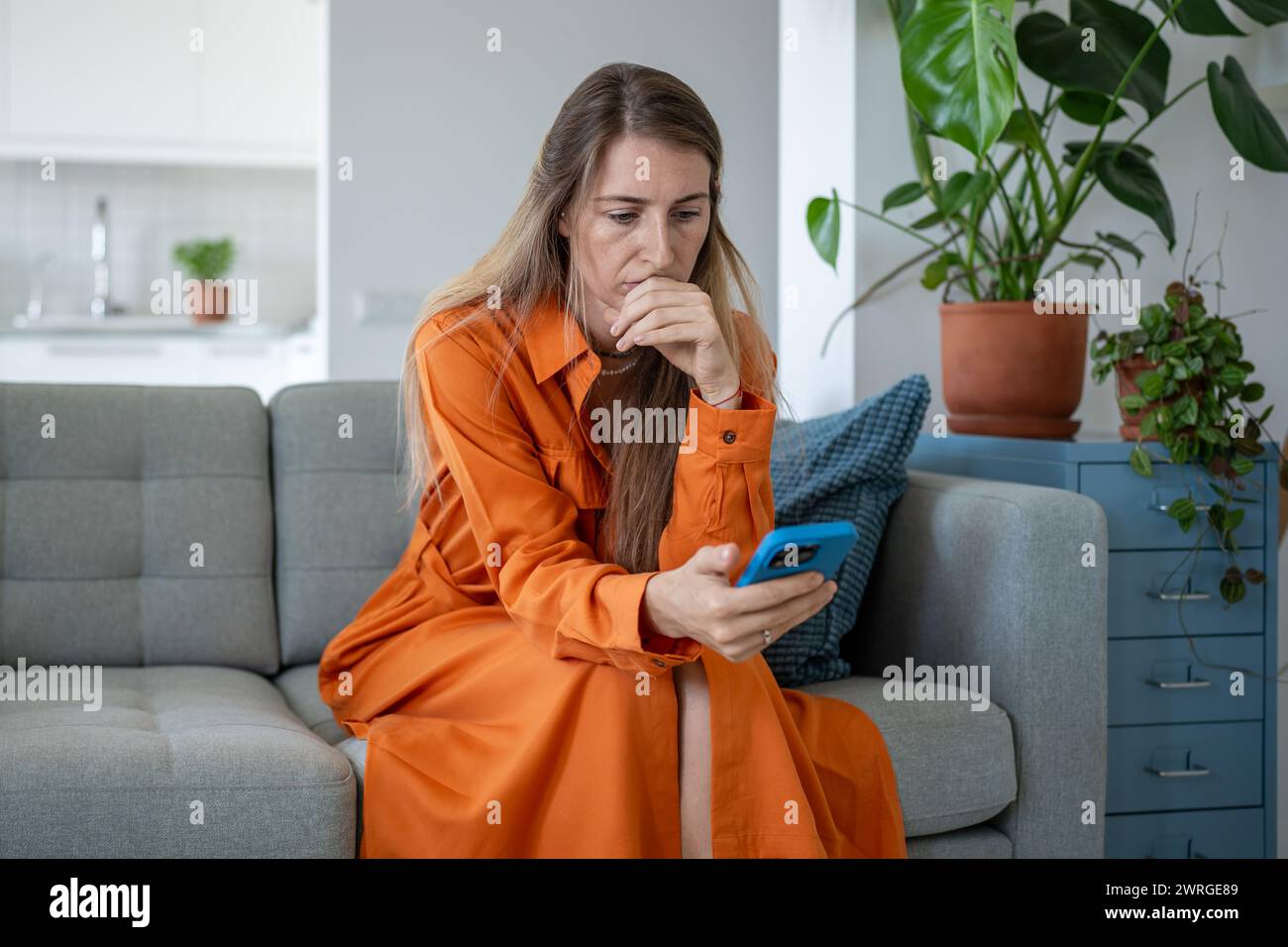 La donna stressata guarda lo schermo dello smartphone premendo nervosamente il palmo sulle labbra, leggendo notizie spiacevoli. Foto Stock
