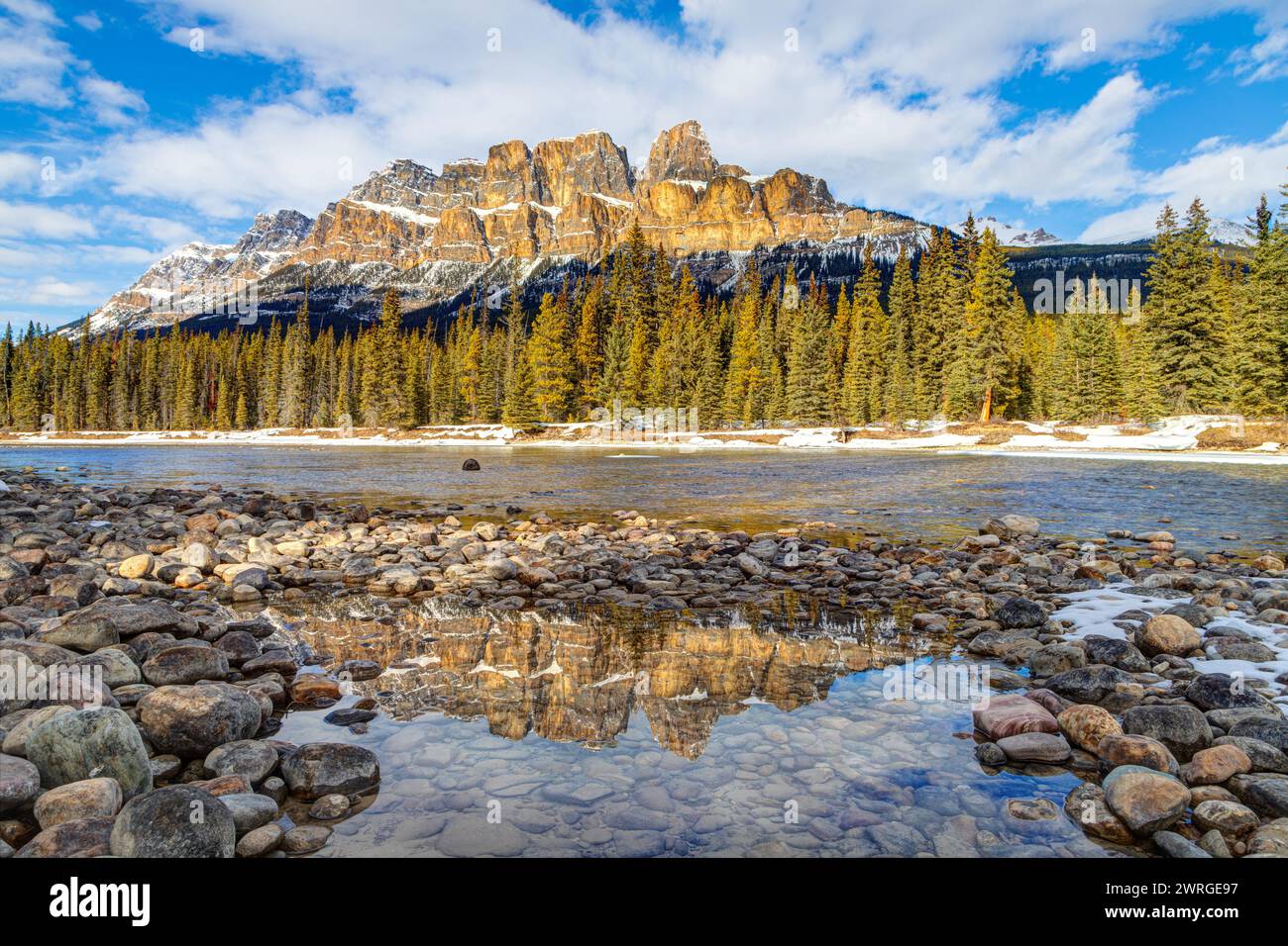 Il sole del tardo pomeriggio si riflette sulla maestosa Castle Mountain nel Parco Nazionale di Banff, Canada, con riflessioni sulle pozzanghere innevate lungo il fiume Bow Foto Stock