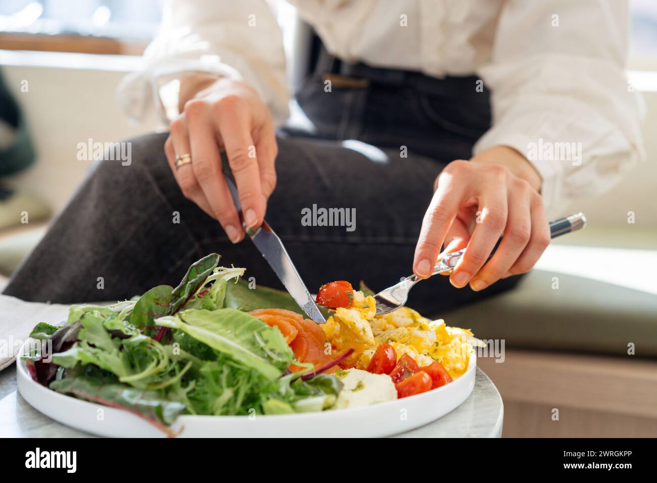 Primo piano di una donna che mangia un piatto sano di pancake di spinaci, uova strapazzate, salmone, pomodori e lattuga Foto Stock