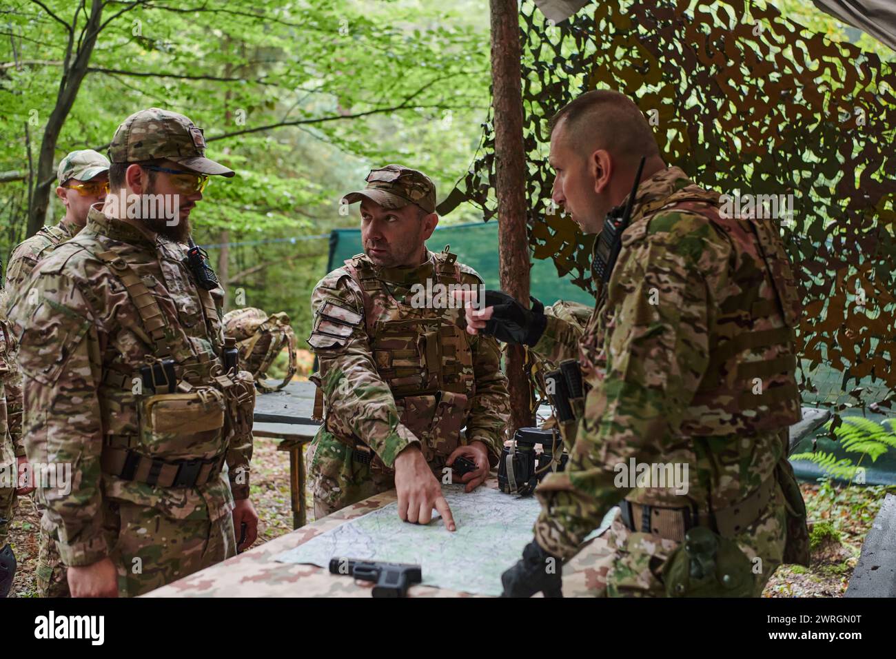 Un'unità militare altamente addestrata pianifica e organizza una missione tattica mentre studia una mappa militare durante una sessione informativa Foto Stock