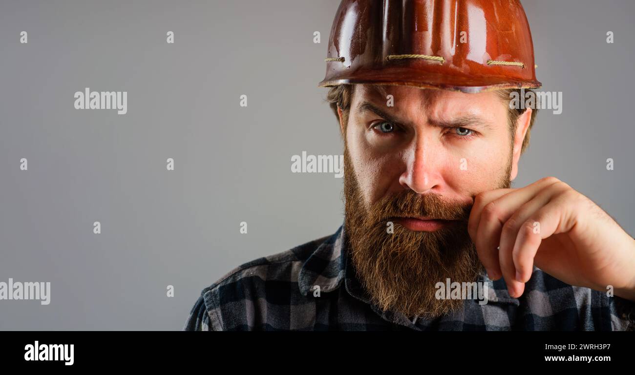 Primo piano ritratto di un operaio edile serio in elmetto. Operaio con barba in camicia a quadri e casco protettivo. Architetto, appaltatore o. Foto Stock