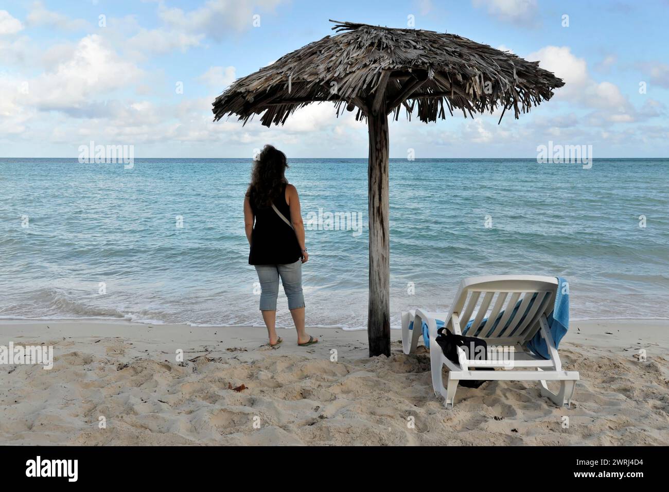 Donna in piedi sotto un ombrellone sulla spiaggia che guarda al mare, Cayo Coco, Cuba, America centrale Foto Stock