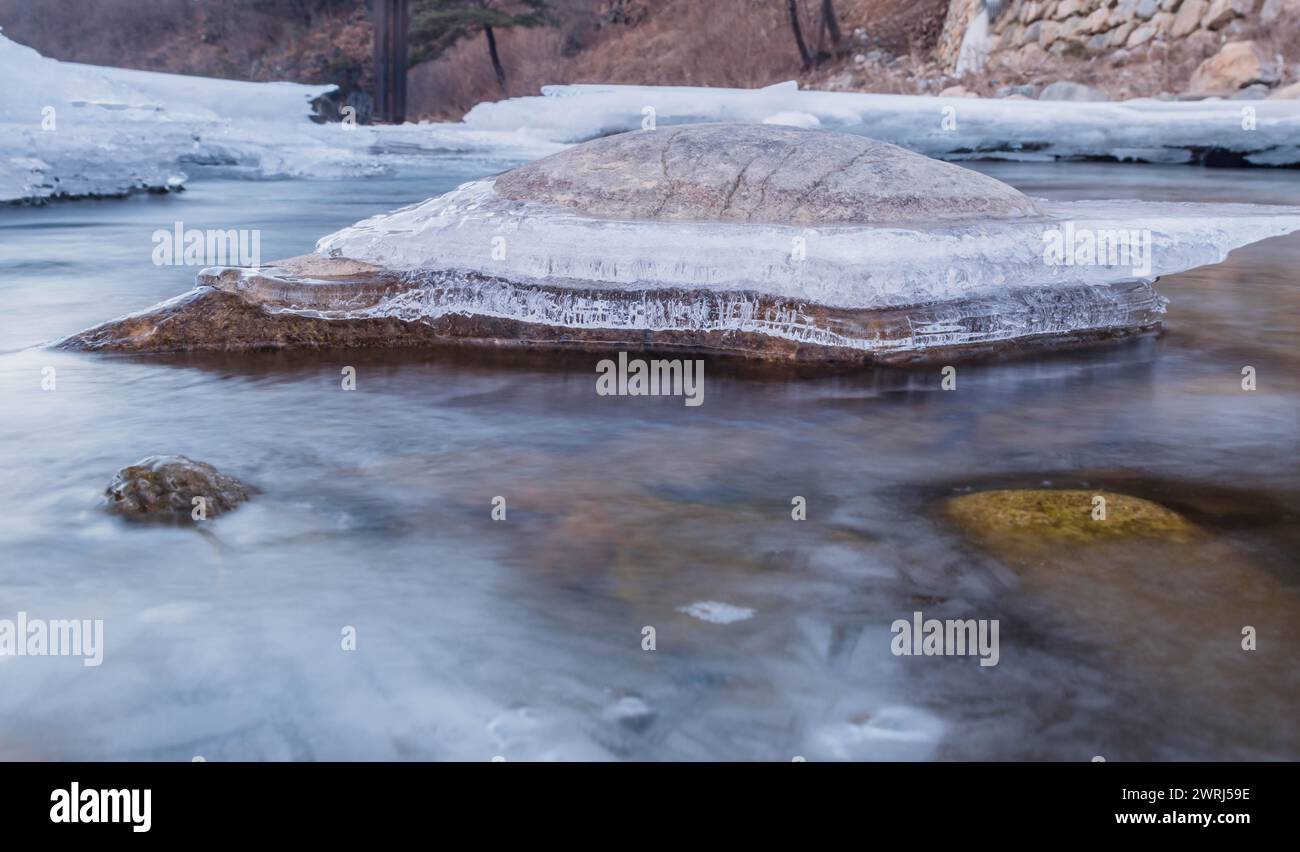 Primo piano di ghiaccio congelato intorno a grandi pietre creando un modello unico e acqua di fiume presa con lunga esposizione nella provincia di Gyeonggi della Corea del Sud Foto Stock