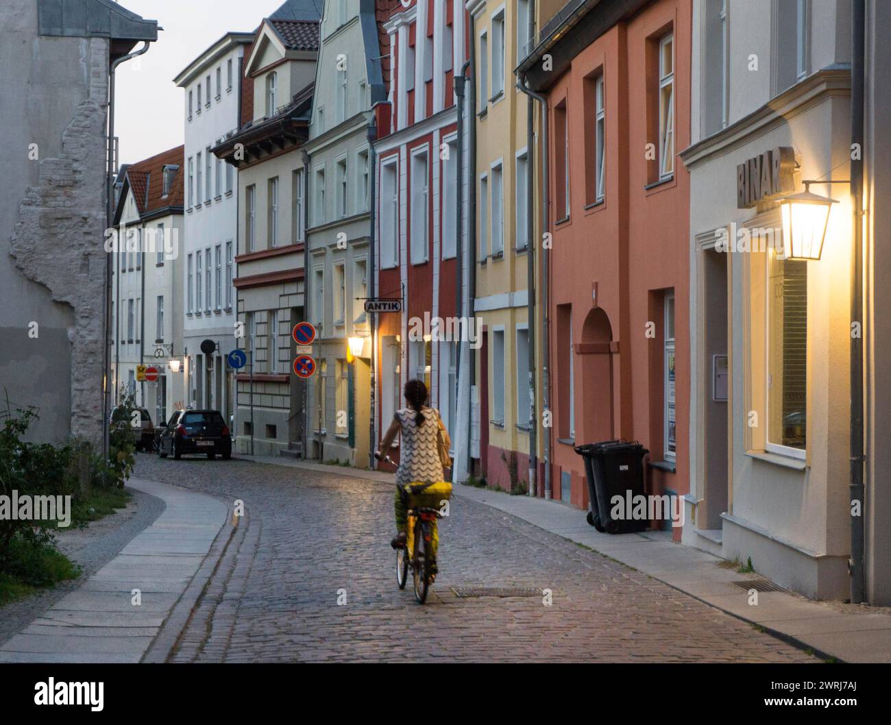 Una donna guida in bicicletta attraverso una strada illuminata da lanterne nella storica città vecchia di Stralsund, 12/09/2016 Foto Stock