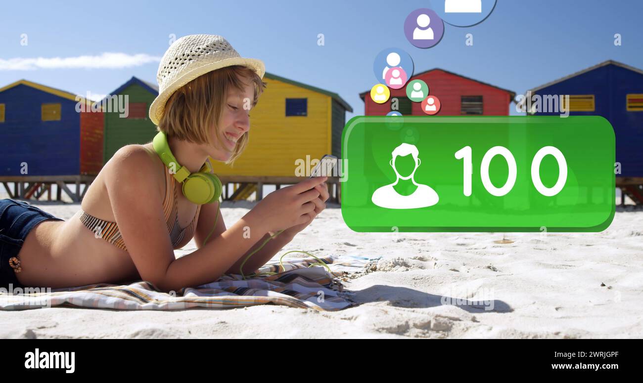 Primo piano di una donna caucasica sdraiata sulla spiaggia con un costume da bagno che digita sul telefono Foto Stock