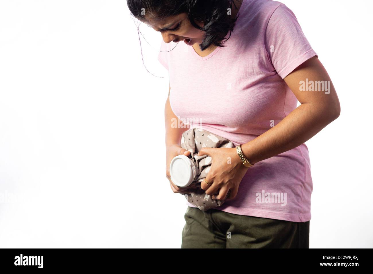 Una donna indiana che applica una borsa di acqua calda sulla pancia per alleviare il dolore su sfondo bianco Foto Stock