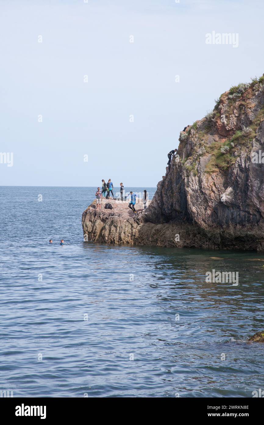 Bambini che saltano dalle rocce in mare a Babbacombe Beach a Torbay, nel Devon, nel Regno Unito Foto Stock
