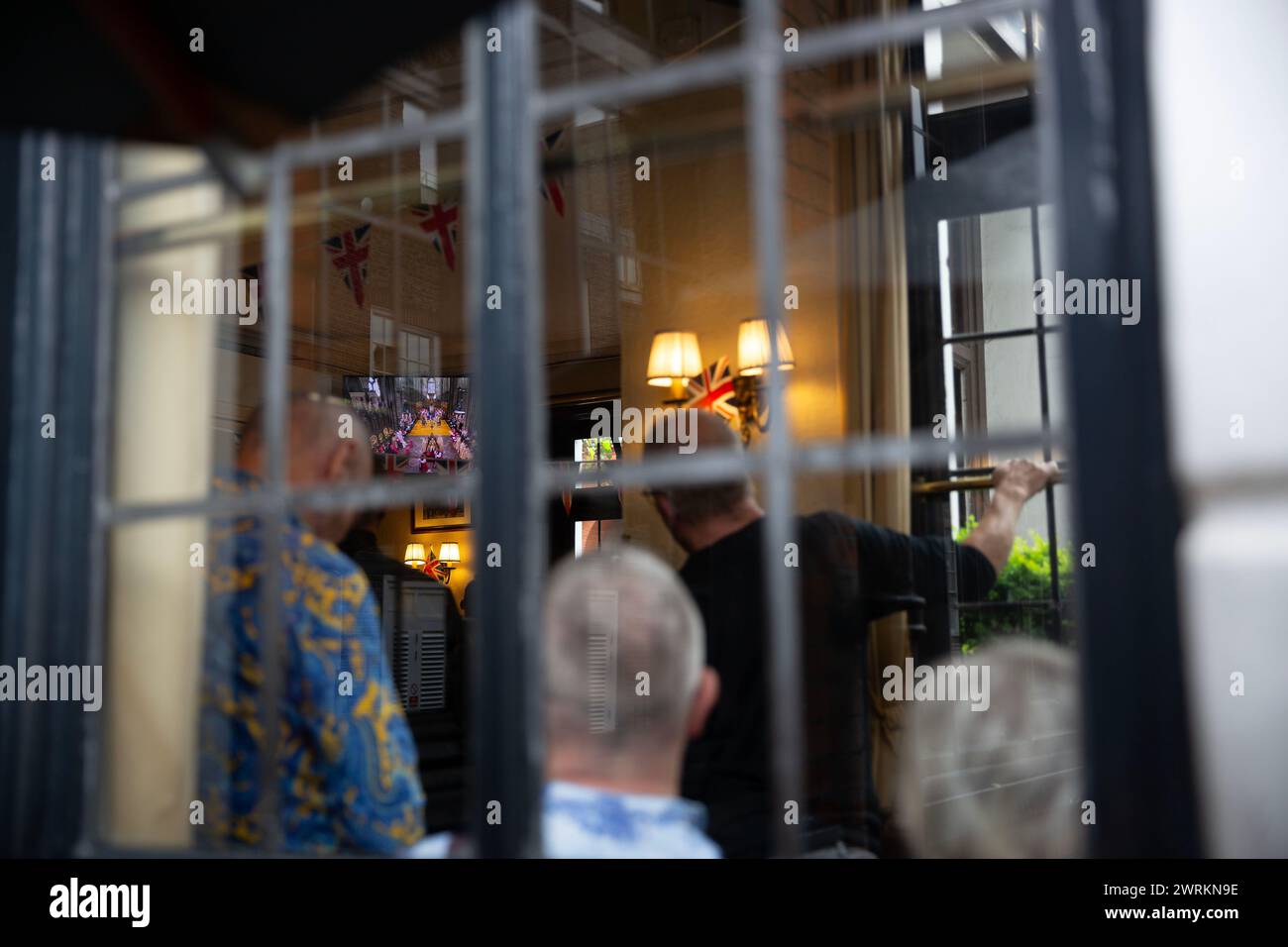 La gente guarda l'incoronazione di re Carlo III sullo schermo in un pub nel centro di Londra. Foto Stock