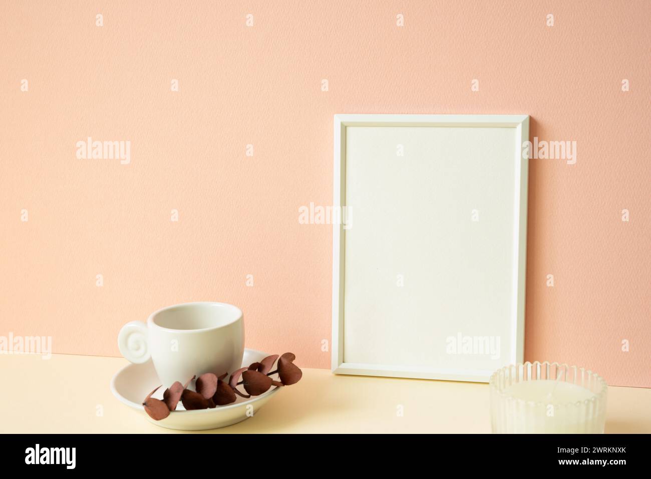 Cornice bianca con tazza da caffè e candela sul tavolo in avorio. sfondo rosa della parete Foto Stock