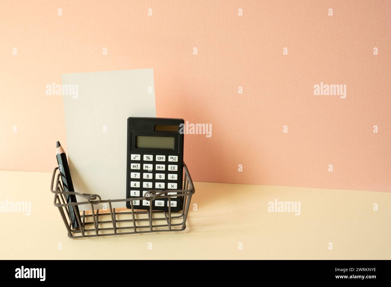 Carrello per gli acquisti consumer con calcolatrice, matita, blocco appunti su sfondo avorio e rosa. Concetto economico Foto Stock