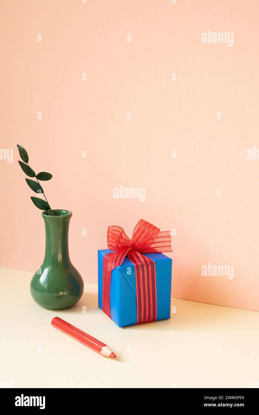 Confezione regalo blu, vaso di foglia di eucalipto, matita rossa su tavolo in avorio. sfondo rosa della parete Foto Stock
