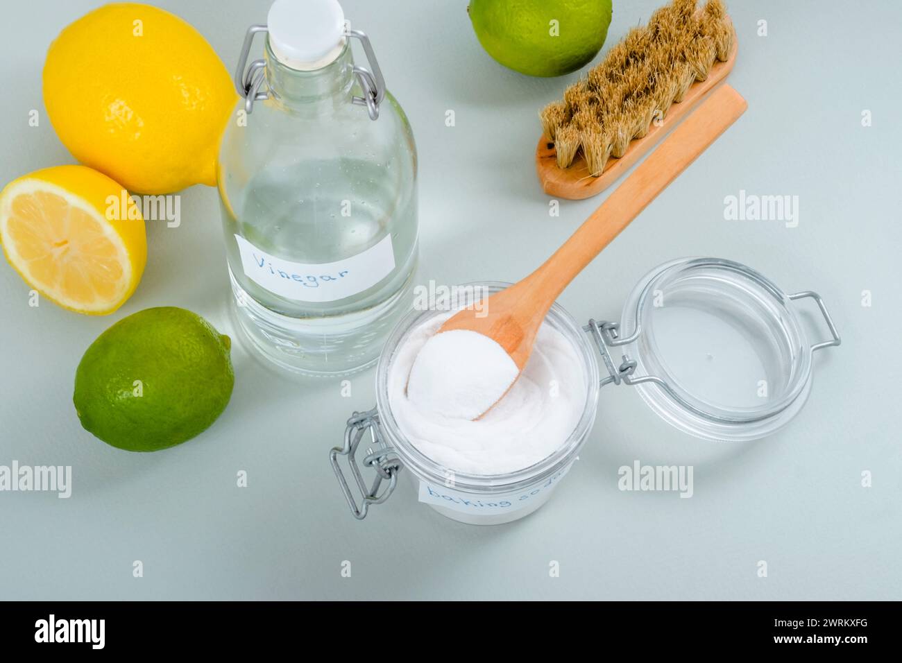 Prodotti naturali per la pulizia della casa bicarbonato di sodio, aceto bianco, agrumi, spazzola su sfondo grigio. Foto Stock
