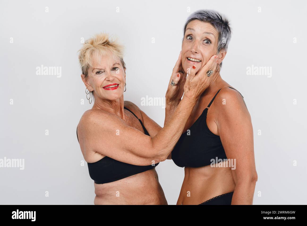 madre adulta matura che posa dando amore a sua figlia, sono in biancheria intima e hanno i capelli corti, indossano lingerie nera, studio girato con ba bianca Foto Stock