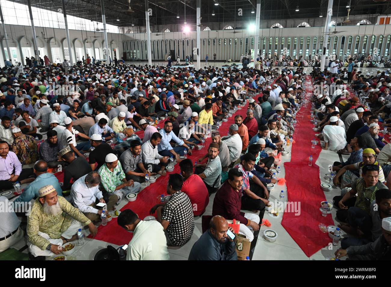 I devoti musulmani si siedono insieme prima di rompere il digiuno durante il mese Santo del Ramadan alla Moschea Nazionale Baitul Mukarram a Dacca, Bangladesh, il 13 marzo 2024 Foto Stock