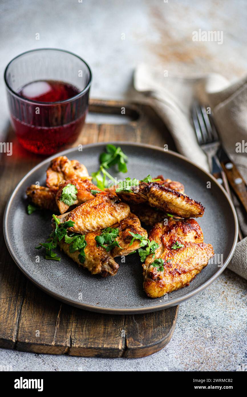 Deliziose ali di pollo arrosto in salsa piccante guarnite con coriandolo fresco. Servito su un piatto grigio con un cocktail di ciliegia a lato. Foto Stock