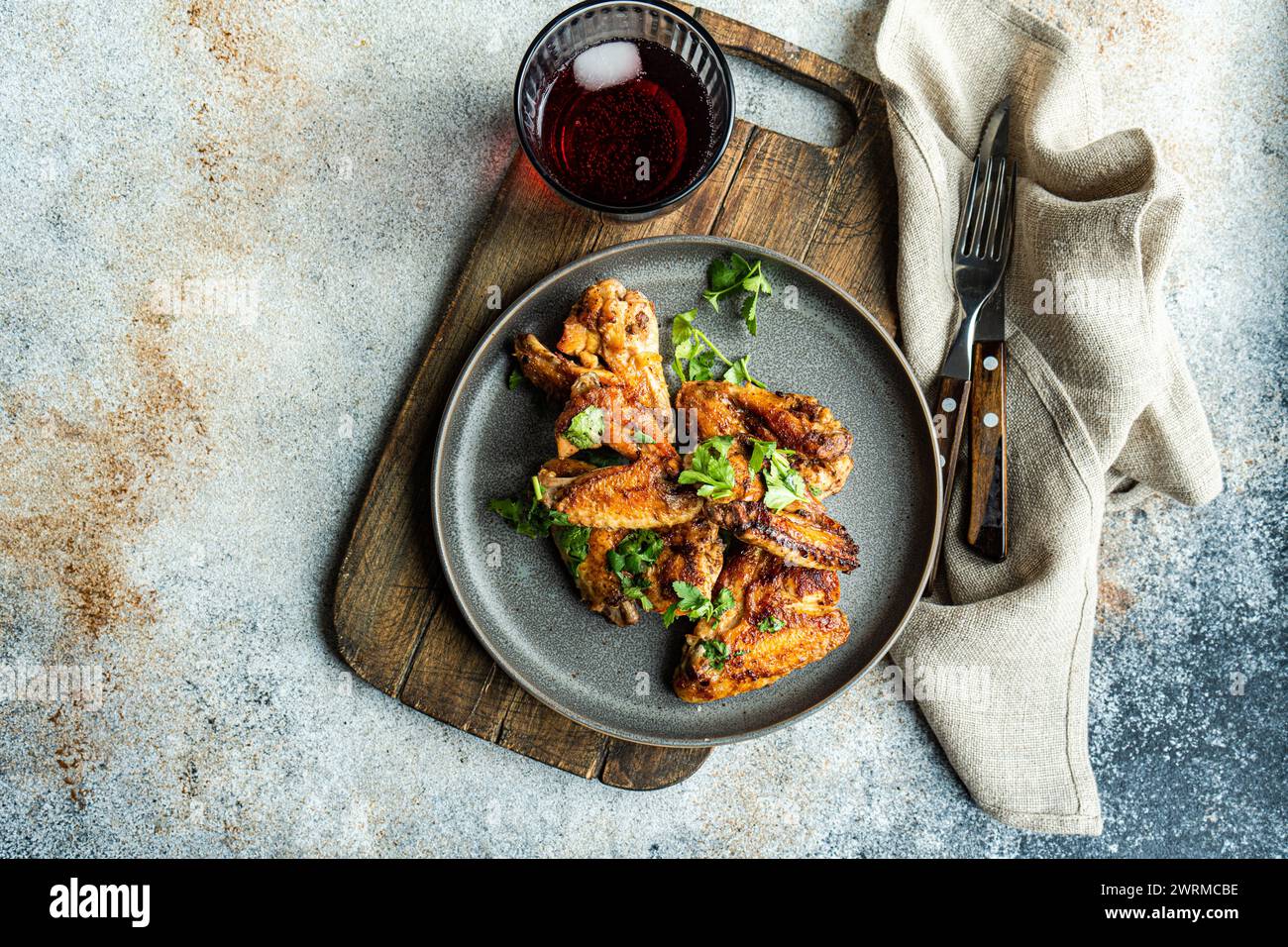 Vista dall'alto ali di pollo arrosto in salsa piccante guarnita con coriandolo fresco, presentato su un piatto accanto a un bicchiere di cocktail di ciliegia, con cutler Foto Stock
