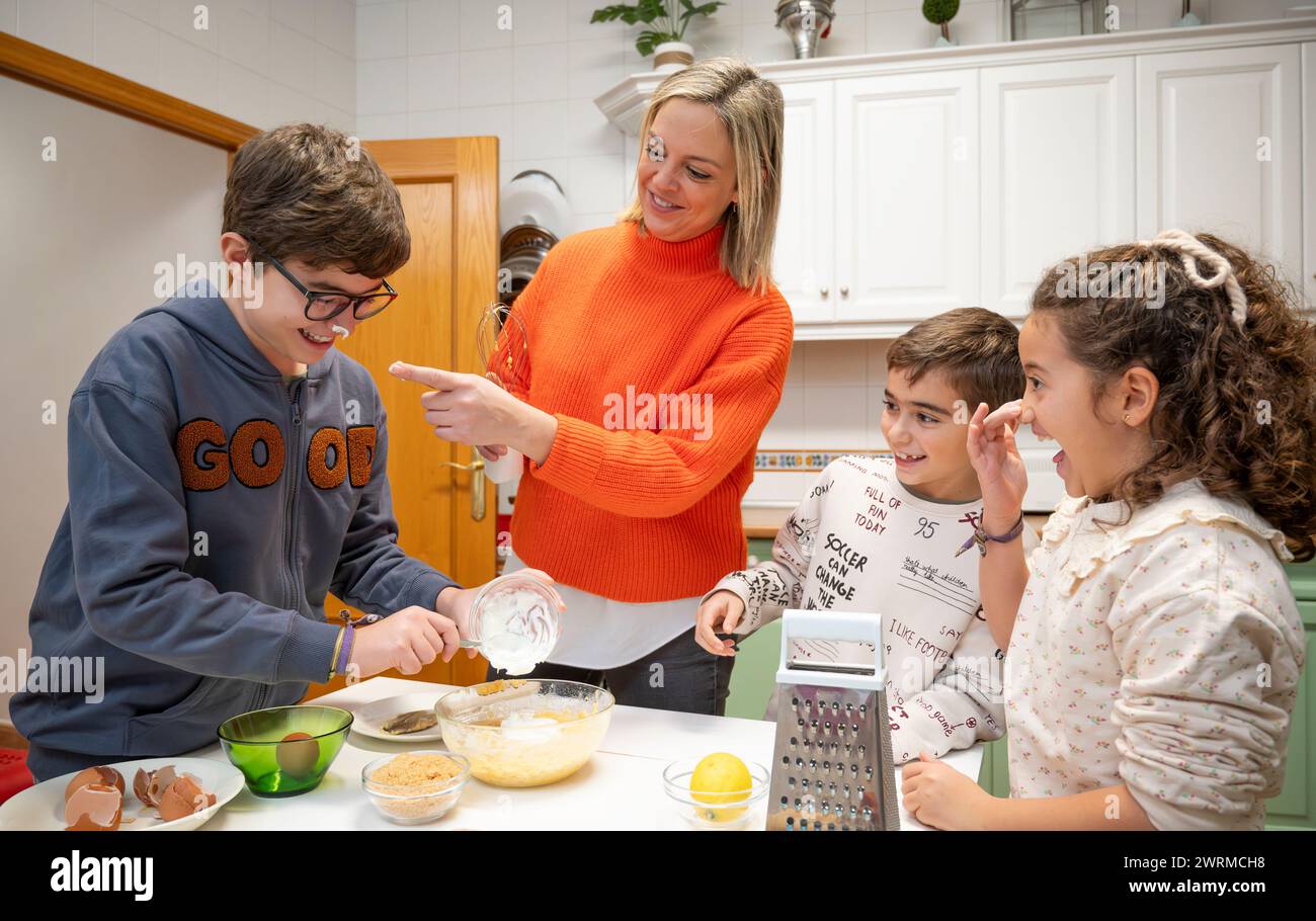 Un gioioso momento in famiglia come madre guida i suoi figli nelle attività di cottura in un'accogliente cucina casalinga, rafforzando il concetto di riunione di famiglia. Foto Stock