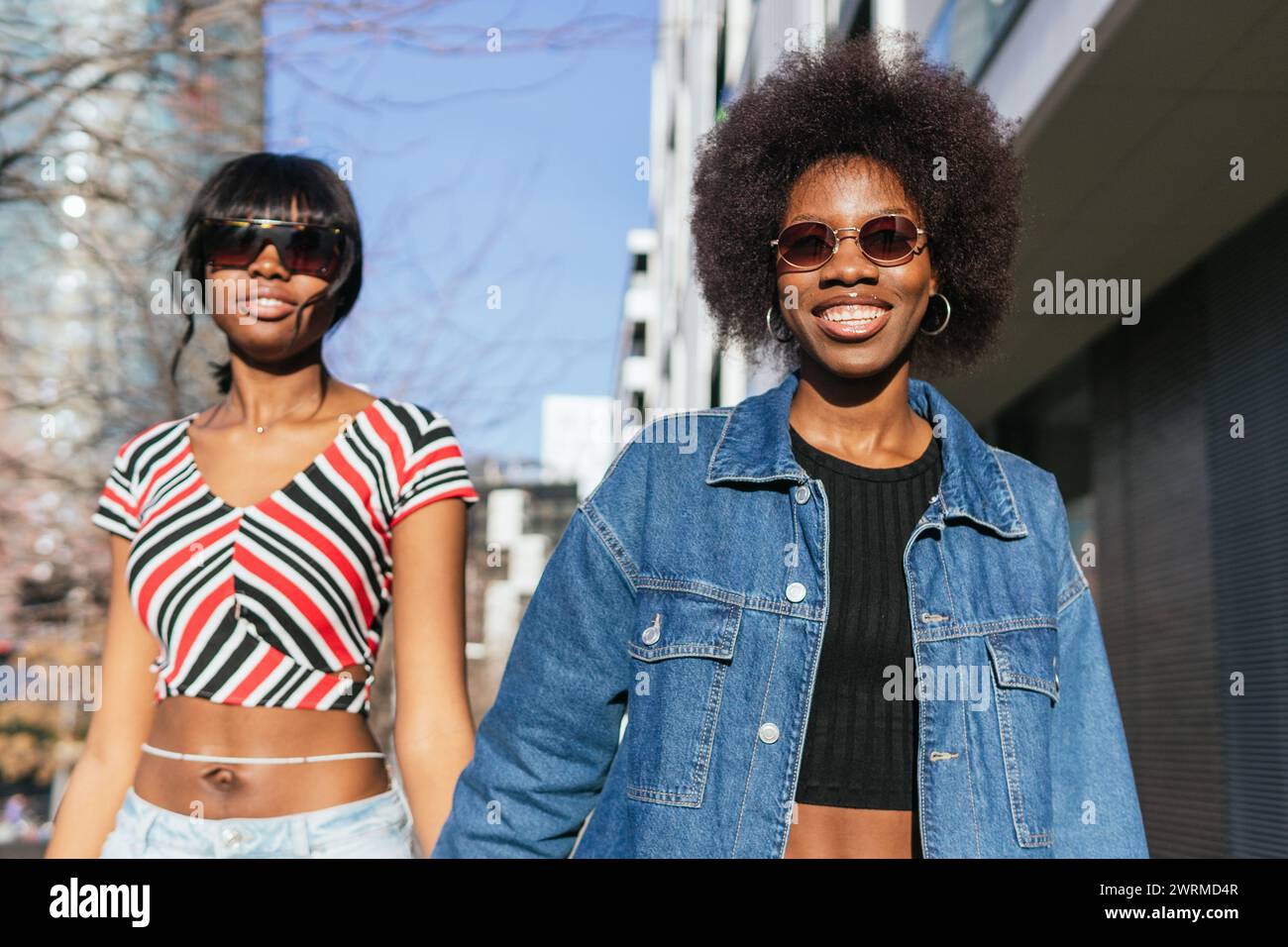 Due eleganti sorelle afroamericane irradiano felicità mentre passeggiano per la città, godendosi la calda luce del sole insieme Foto Stock