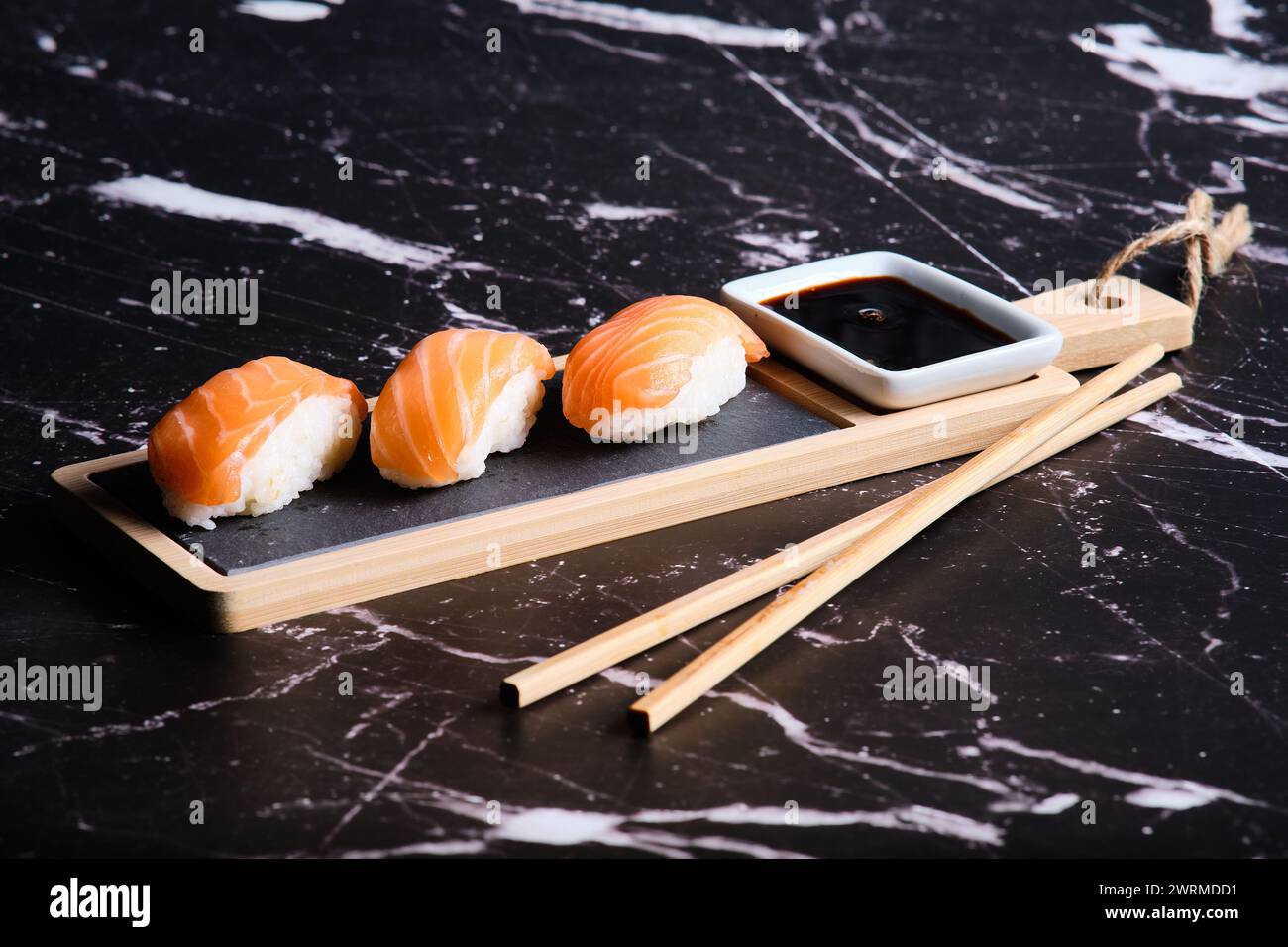 Tre pezzi di sushi di salmone serviti su un tavolo di legno con salsa di soia e bacchette su sfondo marmorizzato. Foto Stock