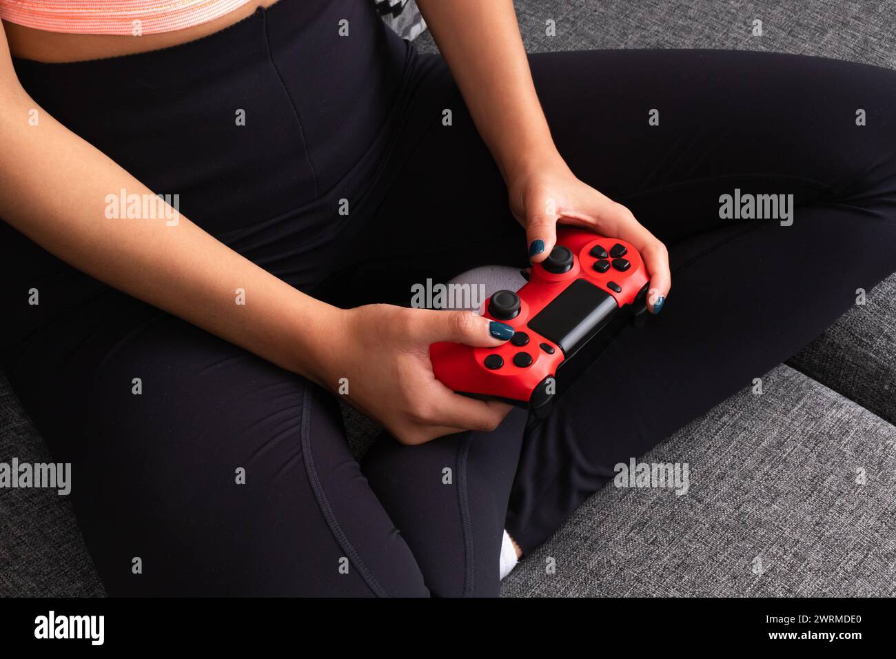 Dall'alto, donna irriconoscibile e corta seduta comodamente con un controller di gioco rosso in mano Foto Stock