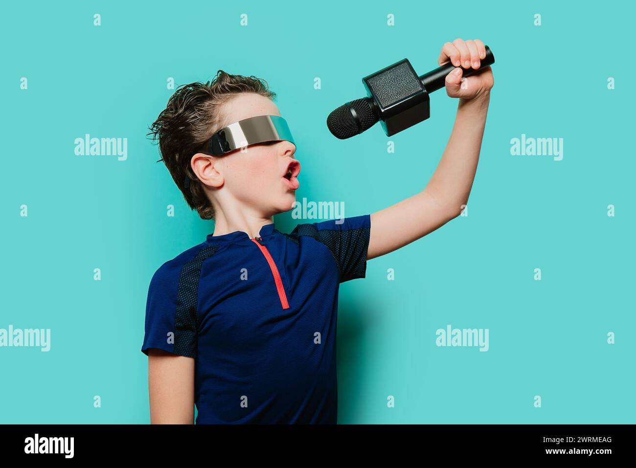 Un ragazzo energico con visiera futuristica e top sportivo sfoggia una melodia, quasi sul palco con uno sfondo color ottanio Foto Stock